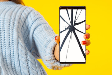 A broken smartphone screen. Replacement of the smartphone screen. Equipment repair service. The girl shows a mobile phone with a cracked screen. Orange background.