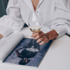 Young woman drinks wine while reads magazine in a bar