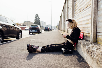 Young woman nonconformist diverse sitting concrete outdoors using smartphone