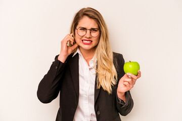 Young business caucasian woman holding an apple isolated on white background covering ears with hands.