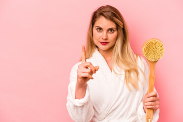 Fototapeta premium Young caucasian woman holding back scratcher isolated on pink background showing number one with finger.