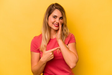 Young caucasian woman isolated on yellow background saying a gossip, pointing to side reporting something.