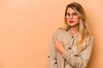 Young caucasian woman isolated on beige background smiling and pointing aside, showing something at blank space.