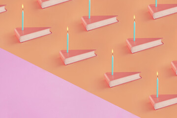 Triangle shaped books with birthday candles on isolated pastel coral-orange background with pink...