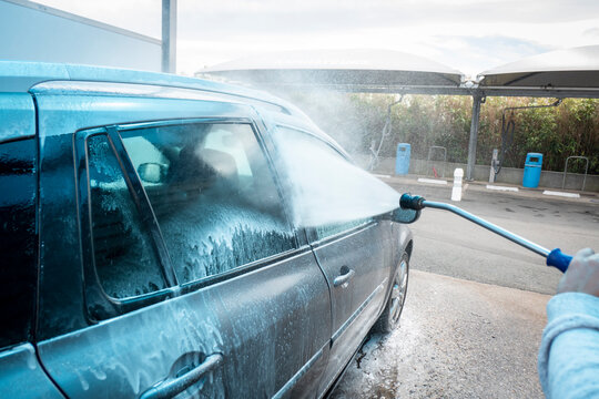 Lavagem de carro com bomba de equipamento de água de alta pressão no auto atendimento ao ar livre. Veículo coberto com detergentes químicos 