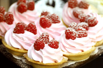 Creamy cakes with fresh raspberries. Sweet desserts in shop window, confectionery production