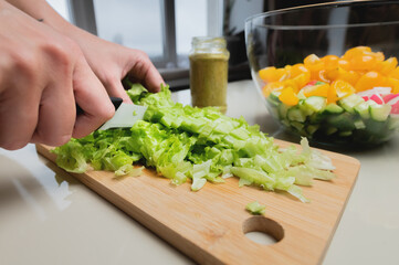 Close-up of a girl's hand cut a salad on a wooden table, a woman prepares a vegetarian salad, healthy food, a knife cuts greens