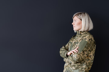 side view of woman in military uniform standing with crossed arms isolated on black.