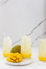 Refreshing drink with mango pulp in glasses with a glass straw on the background of a marble wall, cut mango next to the glass