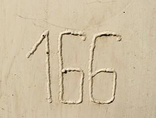 the number 166 is welded on a beige lacquered surface