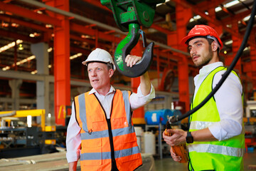 Engineering factory worker control indoor overhead crane to lift up metal construction object on...