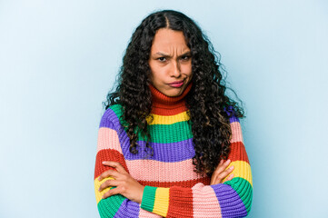 Young hispanic woman isolated on blue background frowning face in displeasure, keeps arms folded.