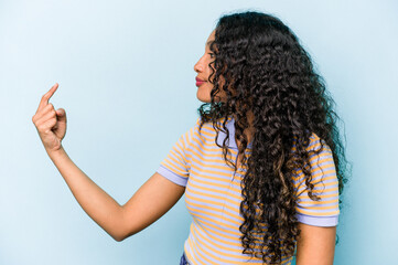 Young hispanic woman isolated on blue background pointing with finger at you as if inviting come closer.