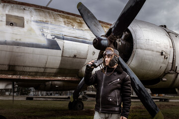 A young manposes in an airplane cemeteryas an old-fashioned pilot.