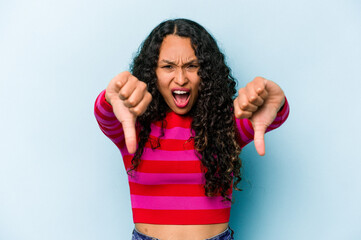 Young hispanic woman isolated on blue background showing thumb down and expressing dislike.