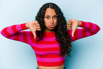 Young hispanic woman isolated on blue background showing a dislike gesture, thumbs down....