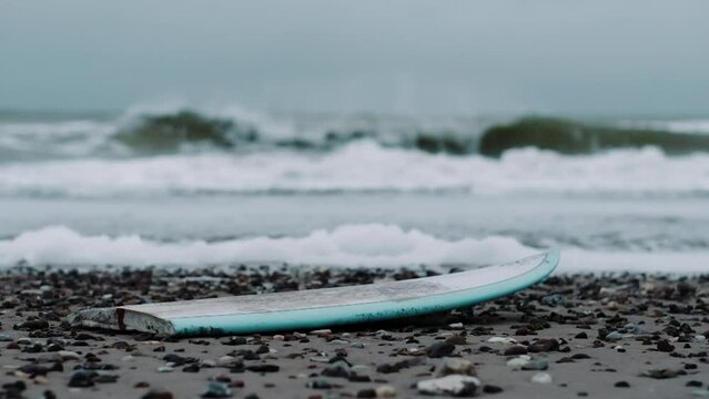 Broken Surfboard Washed Ashore As Sea Rages In Background