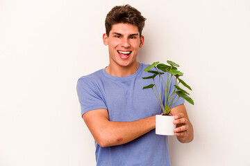 Young caucasian man holding a plant isolated on white background laughing and having fun.