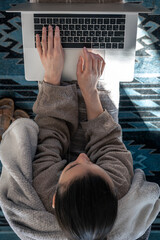 A woman working sitting at a laptop, top view.