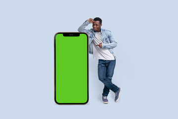 Excited black man standing and pointing Big smartphone with blank green screen, demonstrating copy...