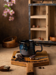 Handmade ceramic coffee mug with coffee beans, hot drink beverage standing on a table. Close up view cozy atmosphere  decorated with blooming sakura.