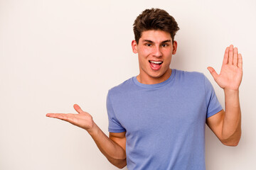 Young caucasian man isolated on white background holds copy space on a palm, keep hand over cheek. Amazed and delighted.