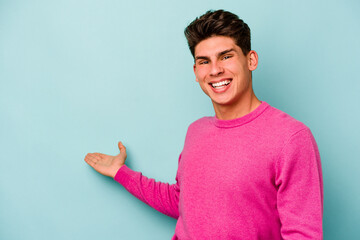 Young caucasian man isolated on blue background showing a welcome expression.