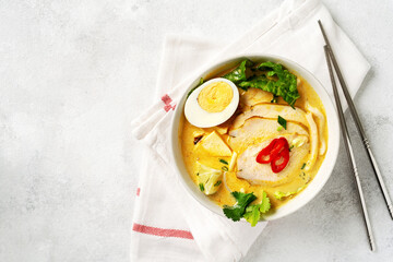 Asian laksa soup with chicken meat in a ceramic bowl on a culinary background. Spicy soup with coconut milk broth, rice noodles and egg in a plate on the kitchen table. Top view from copyspace