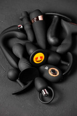 Erotic pleasure toys on a black background. Sex gadgets and masturbation devices. Pink dildo surrounded by black rubber and silicone sex toys: anal butt plugs, vibrators, vaginal balls. Top view.