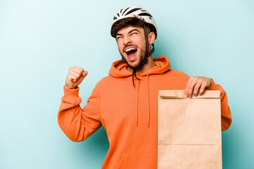 Young hispanic man wearing a helmet bike holding a take away food isolated on blue background...