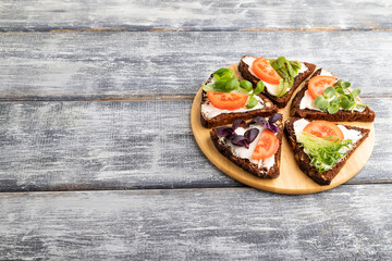 Grain rye bread sandwiches with cream cheese, tomatoes and microgreen on gray. side view, copy space.