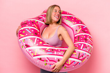 Obraz na płótnie Canvas Young caucasian woman holding an air mattress isolated on pink background looks aside smiling, cheerful and pleasant.