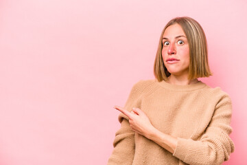 Young caucasian woman isolated on pink background smiling and pointing aside, showing something at blank space.