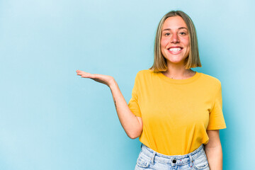 Young caucasian woman isolated on blue background showing a copy space on a palm and holding another hand on waist.