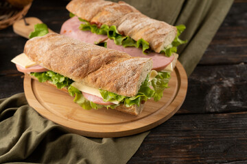 Two fresh sandwiches with ham, cheese, lettuce, on a wooden cutting board.