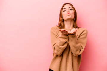 Young caucasian woman isolated on pink background folding lips and holding palms to send air kiss.