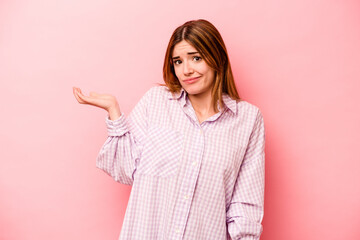 Young caucasian woman isolated on pink background doubting and shrugging shoulders in questioning gesture.