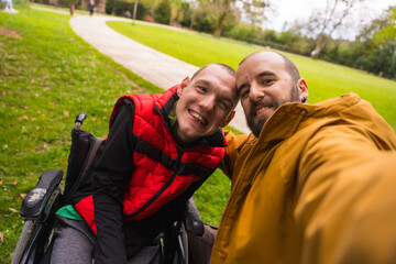 Selfie of a person with a disability in a wheelchair with a friend on a bench in a public park in...