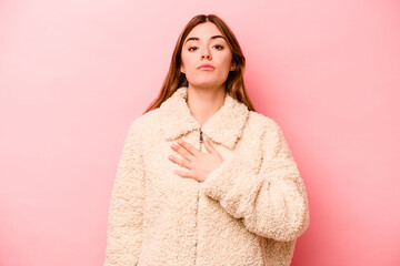 Young caucasian woman isolated on pink background taking an oath, putting hand on chest.