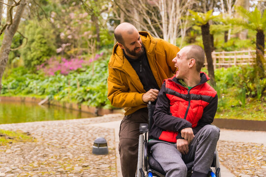 a person with a disability in the wheelchair being pushed by a friend in a public city park, having fun in spring