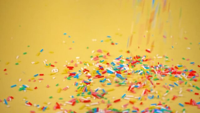 colorful sprinkles falling on yellow background, decoration for cake and bakery, slow motion