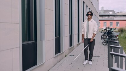 Young asian blind man with using safety stick for walking alone outdoors. Male person wearing glasses and casual clothes. Independence concept.