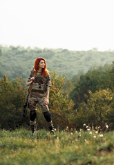 Sniper girl in a green field. Military snipers. The sniper smokes. Red-haired girl in camouflage. Fighting
