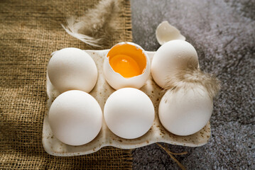 fresh white chicken farm eggs with feathers in a ceramic box on a brown burlap cloth stand on a gray neutral background 2