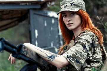 Sniper girl in a green field. Military snipers. The sniper smokes. Red-haired girl in camouflage. Fighting