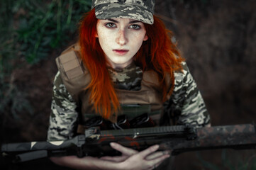 Sniper girl in a green field. Military snipers. The sniper smokes. Red-haired girl in camouflage. Fighting
