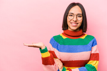 Young hispanic woman isolated on pink background showing a copy space on a palm and holding another...