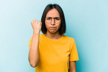 Young hispanic woman isolated on blue background showing fist to camera, aggressive facial...