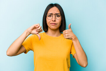 Young hispanic woman isolated on blue background showing thumbs up and thumbs down, difficult...