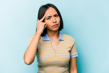 Young hispanic woman isolated on blue background pointing temple with finger, thinking, focused on a task.